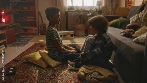 Side full footage of little Caucasian boy sharing secret with his African American best friend, boy giving oath to keep secret by raising left hand and drawing cross on heart in retro living room 90s
