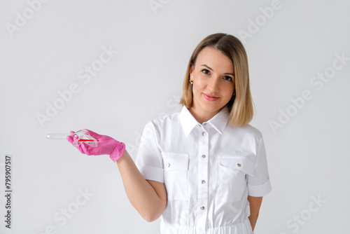 A beautiful sweet woman gynecologist holds a speculum in hand. A female doctor in pink gloves on a white background. Medical examination and prevention of gynecological diseases