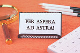 Per aspera as astra in English means through hardships to the stars there is a magnifying glass, a calculator, and pencils on a white business card next to it