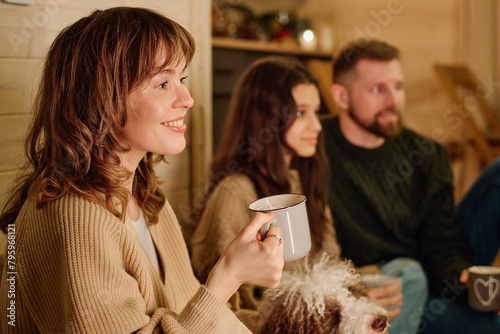Happy Caucasian woman holding mug enjoying spending winter evening with her husband and daughter at home, copy space