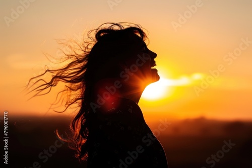 A silhouette of a person laughing against a sunset.