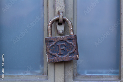 Street photo. Old barn lock with English letter F and pattern hangs on closed blue door close-up. Farm gate. Concept of closure, access, work, guarding, warehouse, storage, information, delivery