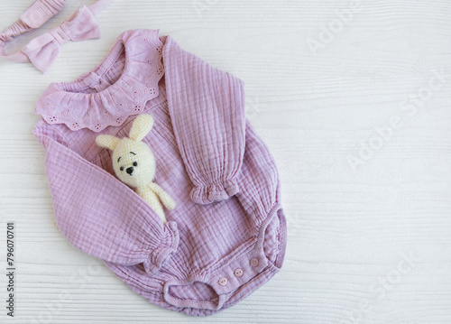 Pink  bodysuit with toy knitted toy and headband. Set of baby clothes and accessories summer on white wooden background. Fashion newborn. Flat lay, top view.