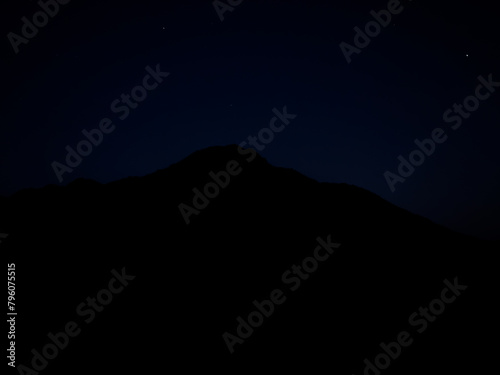 Silhouette of mountain at night with starry sky background.