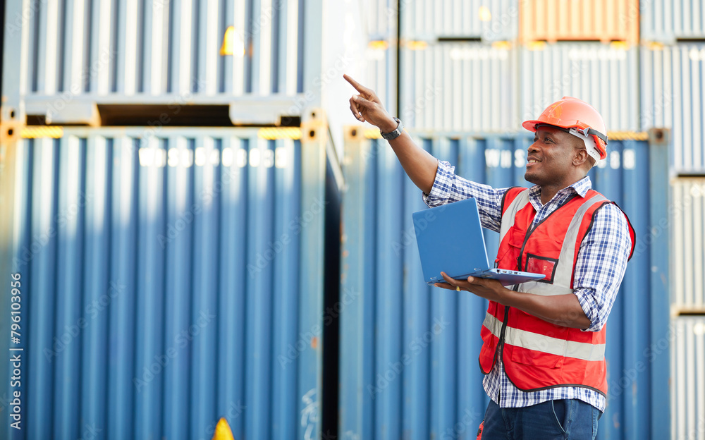 African factory worker or engineer working on laptop computer and pointing pose in containers warehouse storage African factory worker or engineer working on laptop computer and pointing pose in containers warehouse storage