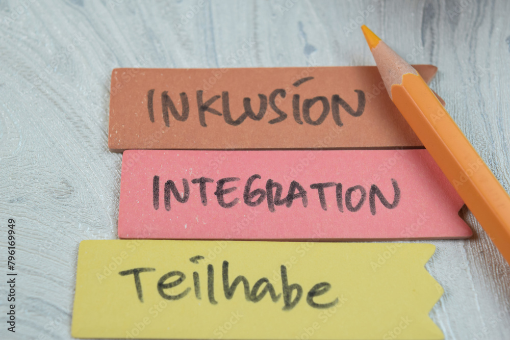 Concept of Inklusion, Integration, Teilhabe write on sticky notes isolated on Wooden Table. Concept of Inklusion, Integration, Teilhabe write on sticky notes isolated on Wooden Table.