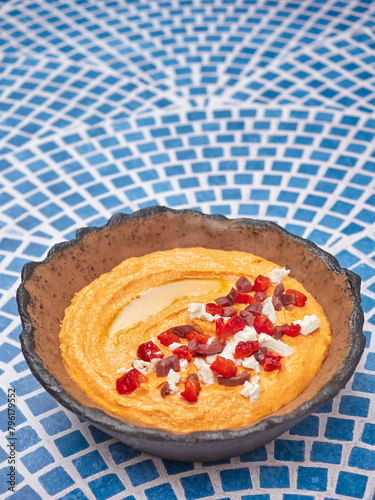 Htipiti, a Greek appetizer based on feta cheese and roasted red peppers, in a ceramic bowl, on a blue and white mosaic table