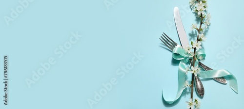 Silver cutlery with blossoming tree branch on blue background with space for text