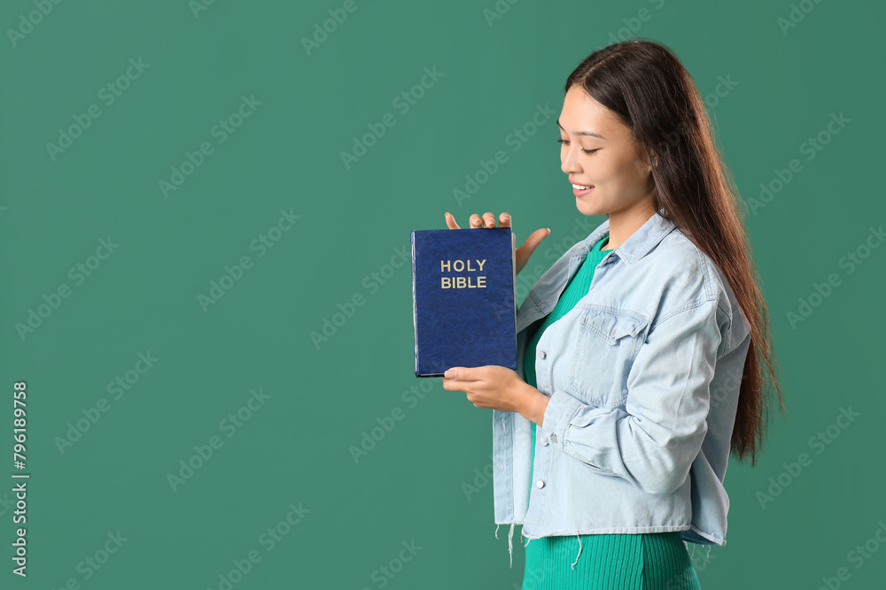 Beautiful young Asian woman with Bible on green background Beautiful young Asian woman with Bible on green background