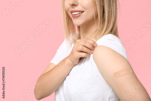 Young woman with medical patch on arm against pink background. Vaccination concept photo