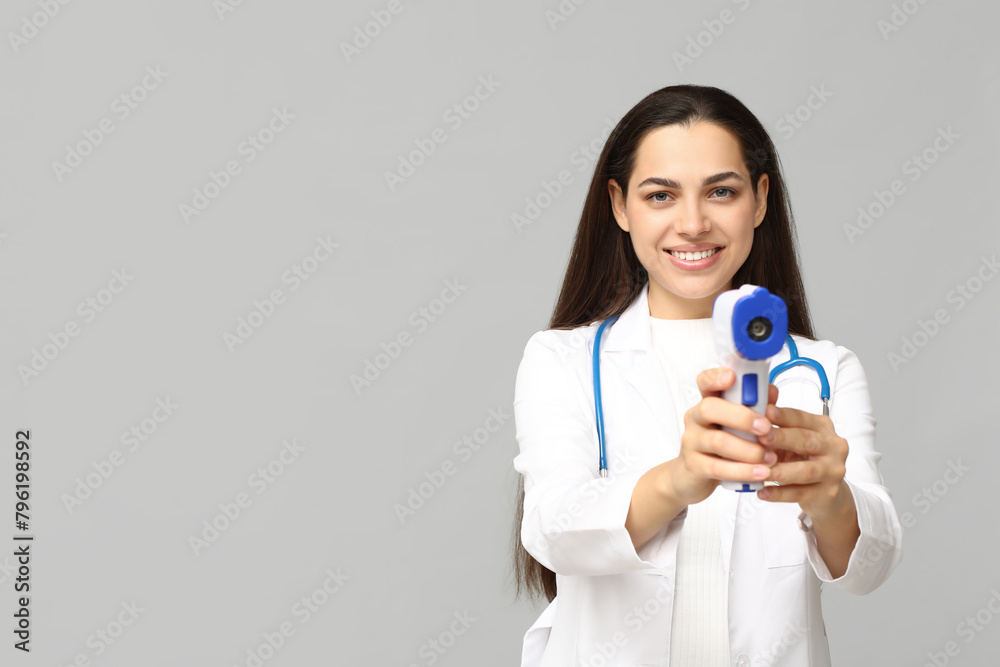 Portrait of female doctor with infrared thermometer on grey background Portrait of female doctor with infrared thermometer on grey background