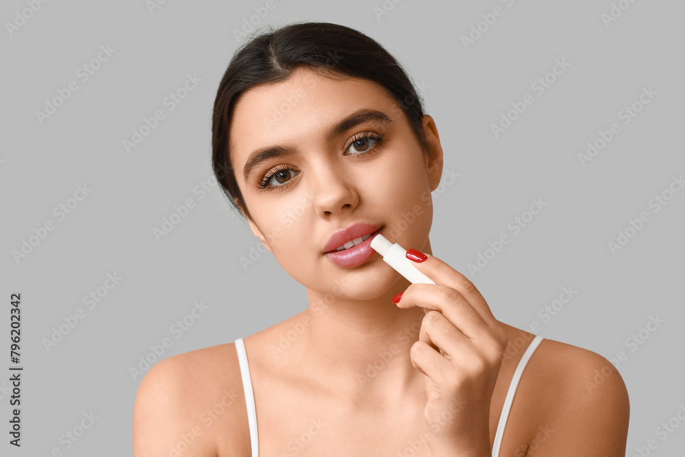 Beautiful young woman applying lip balm on grey background Beautiful young woman applying lip balm on grey background