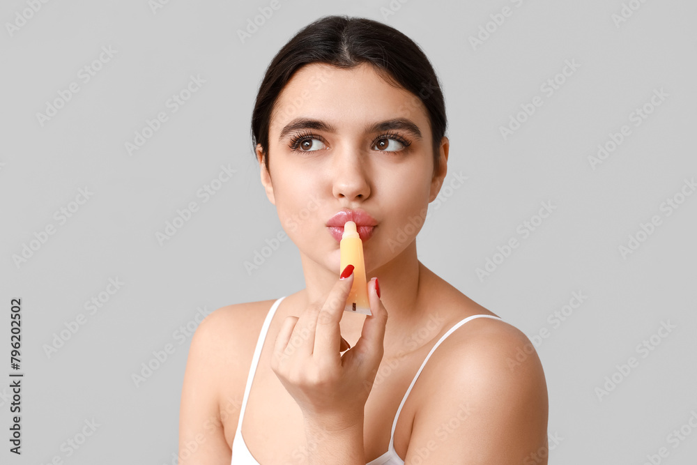 Beautiful young woman applying lip balm on grey background Beautiful young woman applying lip balm on grey background