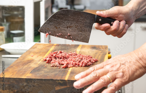 Cook chopping raw beef with a rustic kitchen cleaver on a wooden butcher block to make tartare, ground meat or minced meat, copy space, selected focus