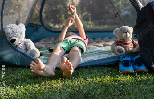 barefoot child is sleeping or relaxing while lying in a tent with his favorite teddy bear. Healthy lifestyle, little tourist, family vacation in nature, summer fun. Interesting childhood