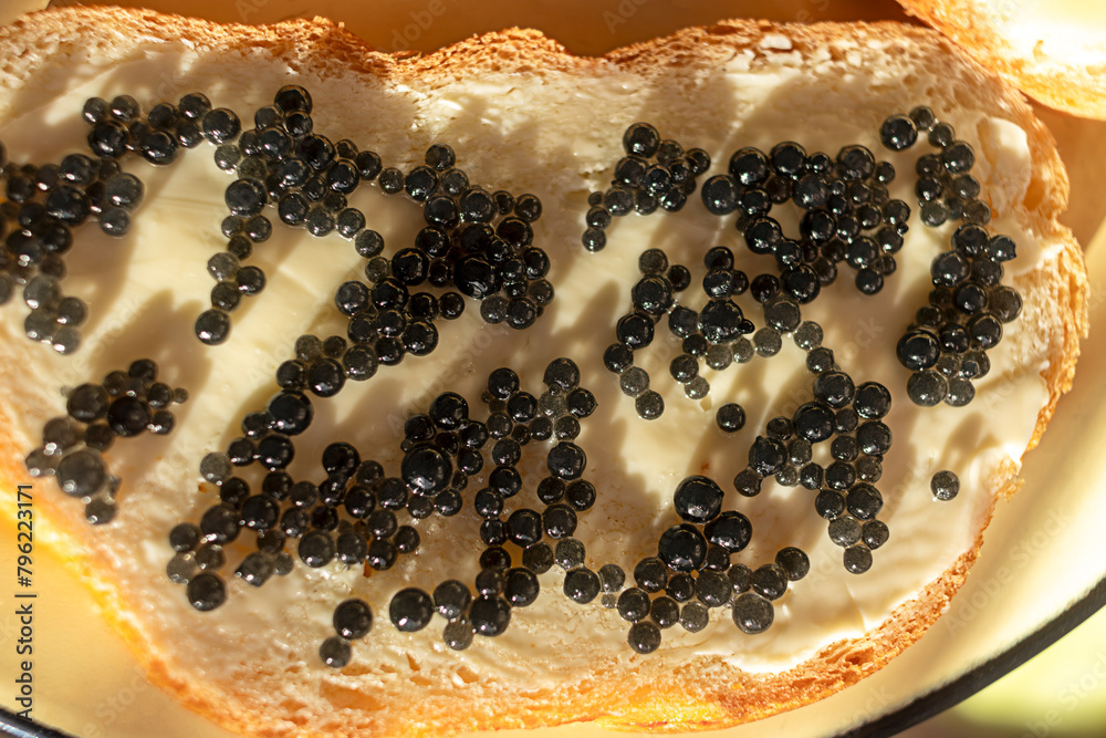 Fototapeta premium White bread sandwich with black grain sturgeon caviar, illuminated by sun on plate. Close-up. Top view.
