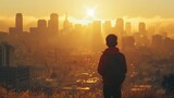 Boy standing on a hill overlooking a city during sunrise