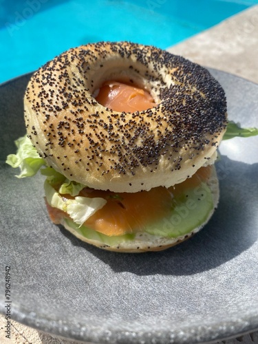 salmon bagel on a plate beside a swimming pool 