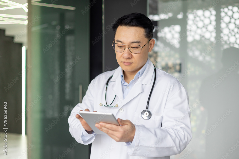 Asian mature doctor reviewing patient records on tablet