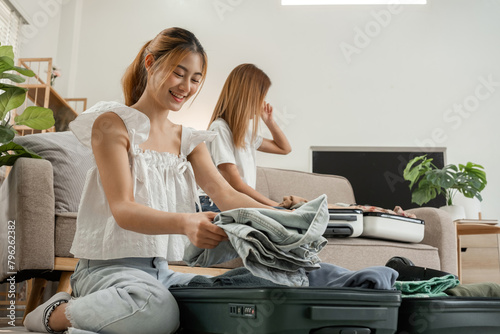 Two young female friends pack a suitcase with clothes and travel passports in preparation for a weekend away.