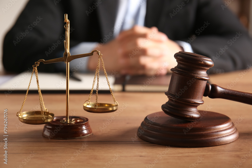 Judge's gavel with scales of justice on table against male lawyer in office Judge's gavel with scales of justice on table against male lawyer in office