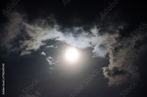 Full moon in the night sky with clouds and rays of light.