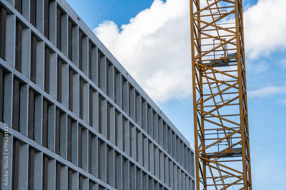 Facade of a new building. Office building with many windows next to a construction crane. Blue sky with white clouds Facade of a new building. Office building with many windows next to a construction crane. Blue sky with white clouds