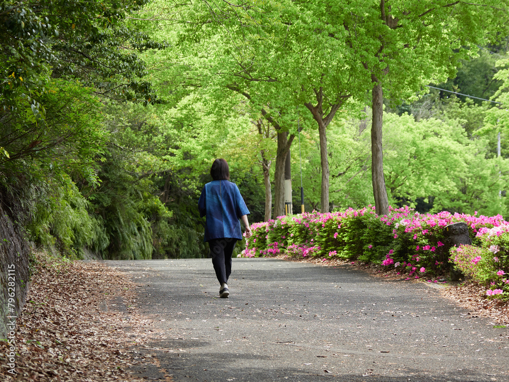 春の新緑の公園の道で散歩する一人の中年女性の姿
