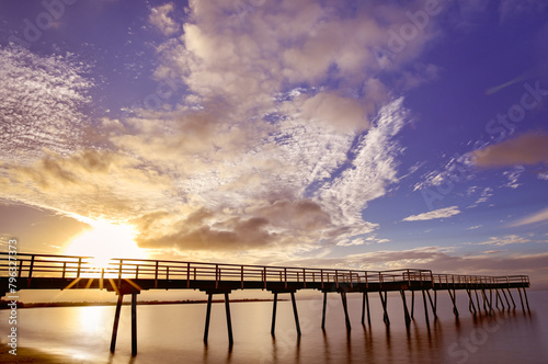 Sunset, Scarness jetty, Hervey Bay, Queensland.  Long exposure, sunburst sunstar, smooth water blue sky and clouds, golden warm summer holiday vacation weekend coastal lifestyle, travel tourism photo