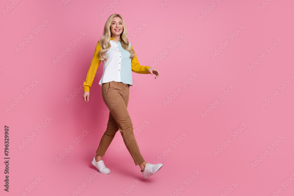 Full length profile portrait of stunning cheerful person walking empty space isolated on pink color background Full length profile portrait of stunning cheerful person walking empty space isolated on pink color background