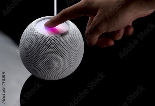 On a smooth surface, a hand presses down on the top of the HomePod, and the HomePod reacts to this and emits a beautiful light photo