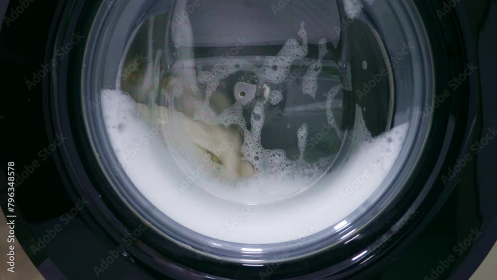 Fast spinning washing machine drum rotating dirty clothes with water during laundry at home Fast spinning washing machine drum rotating dirty clothes with water during laundry at home