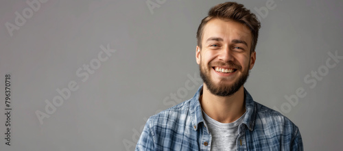 A man with a beard and a blue plaid shirt is smiling. He is wearing a gray shirt. Happy man adult face caucasian isolated background handsome confidence portrait casual attractive guy young person