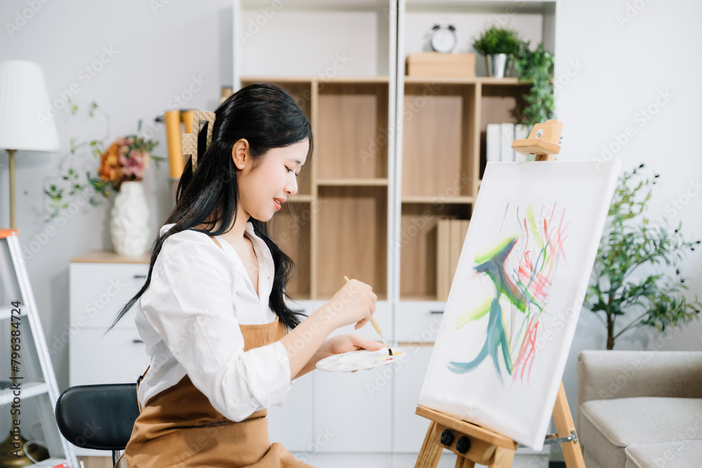 Asian Female painter do artwork in art workshop, painting supplies, oil pastels, two canvas easel, creative space with paintbrush in art studio Asian Female painter do artwork in art workshop, painting supplies, oil pastels, two canvas easel, creative space with paintbrush in art studio