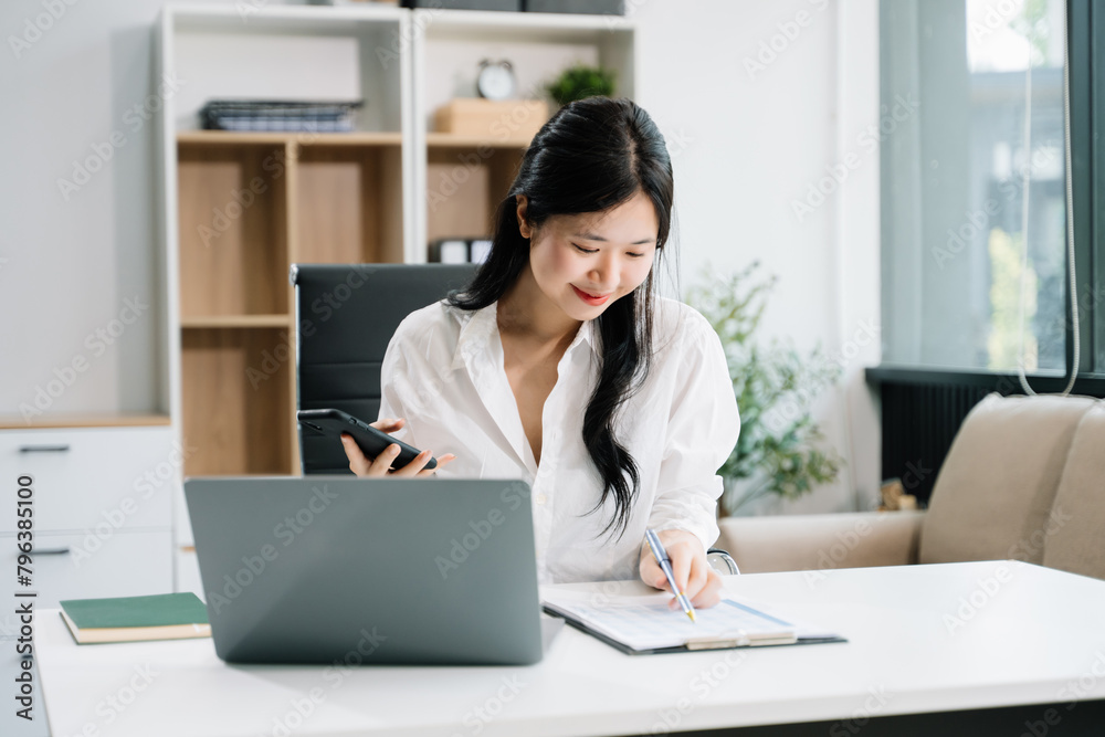 Asian businesswoman typing laptop computer and digital tablet while holding coffee at office