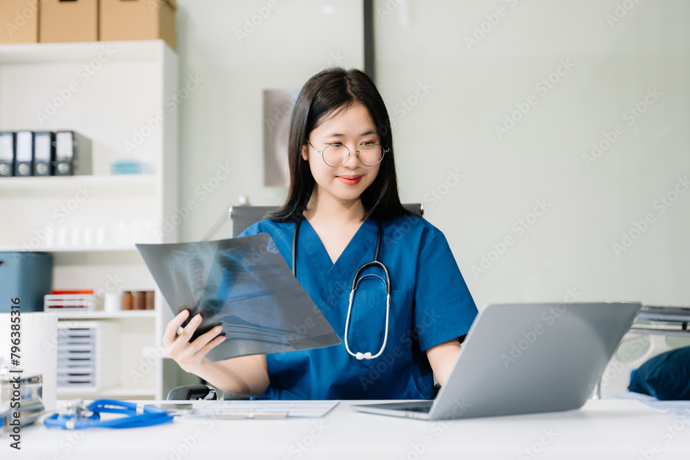 Confident young female doctor in white medical uniform sit at desk working on computer. Smiling use laptop write in medical journal Confident young female doctor in white medical uniform sit at desk working on computer. Smiling use laptop write in medical journal