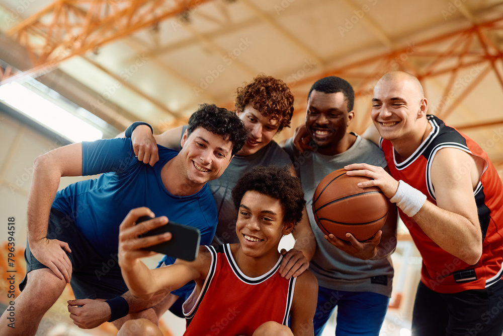 Happy basketball team taking selfie with cell phone on court.