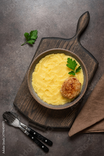 Mashed potatoes with cutlet in a bowl on a wooden board, dark rustic background. Top view, flat lay, vertical