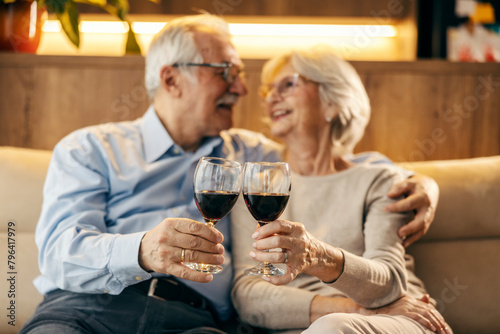 A senior couple is toasting with wine at home and hugging.