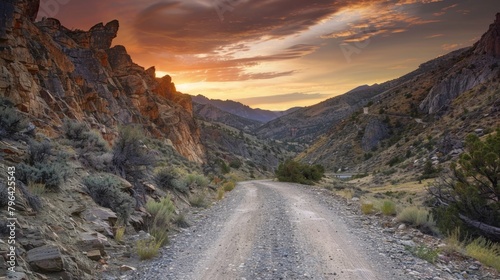 The sun sets over a rocky mountain pass casting a warm glow on the untamed landscape and the unpaved road that leads through it. . AI generation.