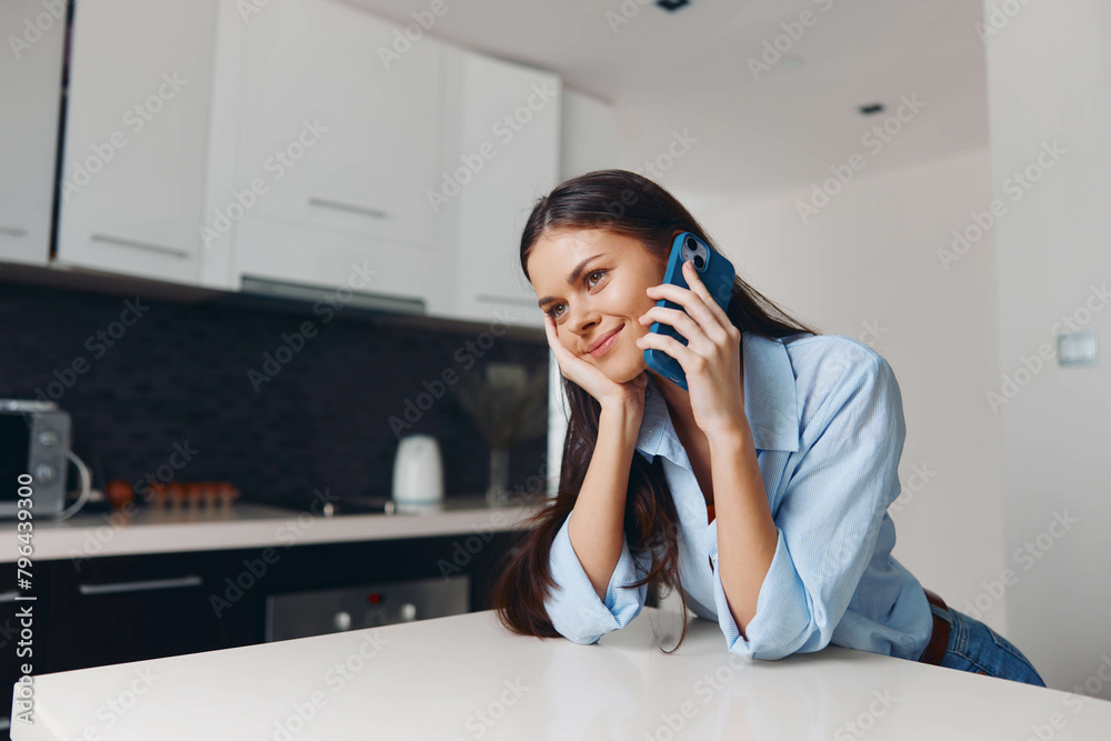 Woman sitting on kitchen counter talking on cell phone while looking at camera in casual home setting Woman sitting on kitchen counter talking on cell phone while looking at camera in casual home setting