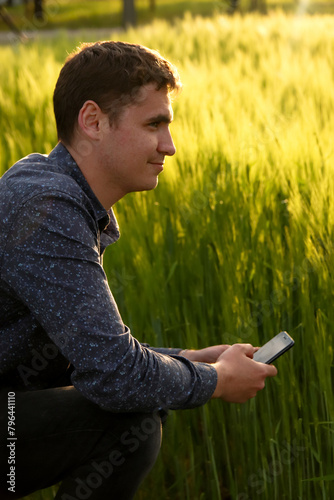 Man with phone on sunset. Young farmer working in a green wheat field, inspecting and tuning irrigation center pivot sprinkler system on smart phone, cell phone