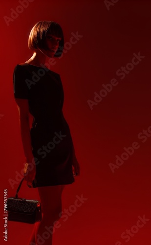 Beautiful young woman in black dress on red background. Studio shot.