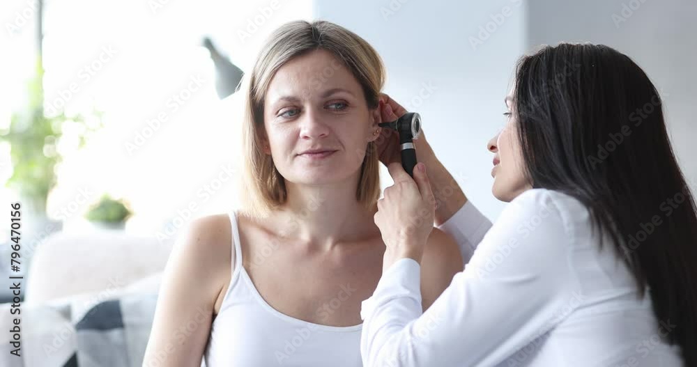 Doctor looking at ear with otoscope to woman patient at home 4k movie. Complications of seasonal colds concept Doctor looking at ear with otoscope to woman patient at home 4k movie. Complications of seasonal colds concept