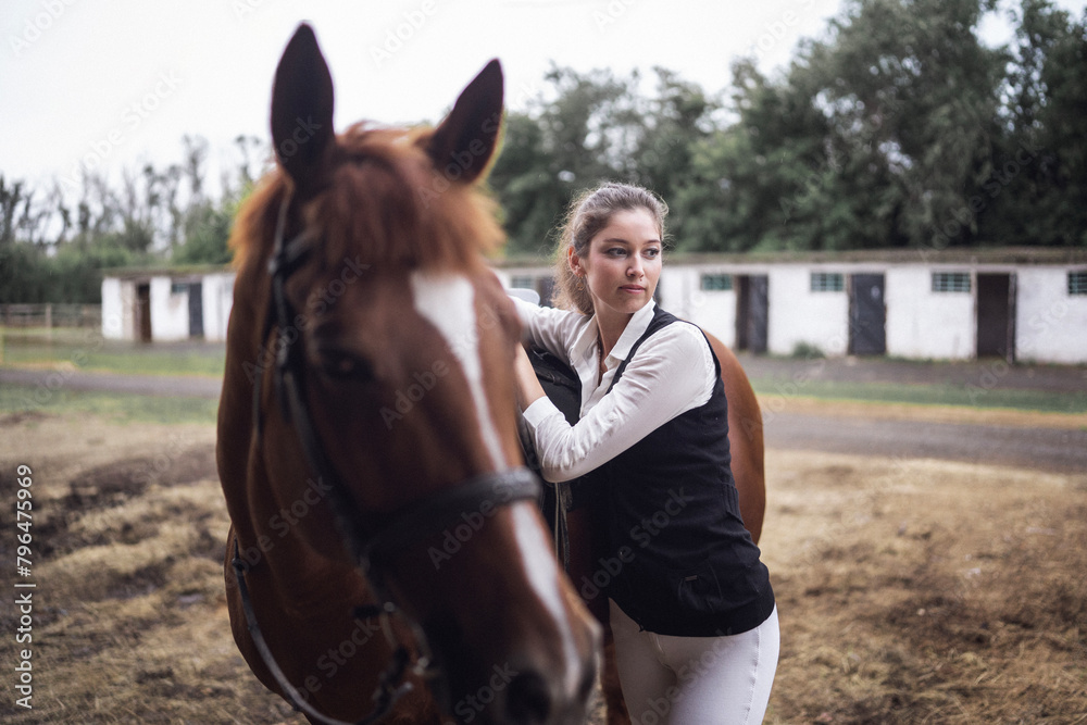 Fototapeta premium A beautiful woman in jockey clothes and a brown horse