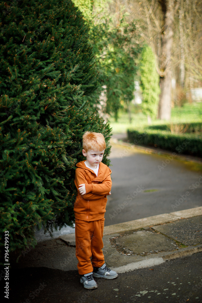 A red-haired boy is walking in a park with lots of greenery A red-haired boy is walking in a park with lots of greenery