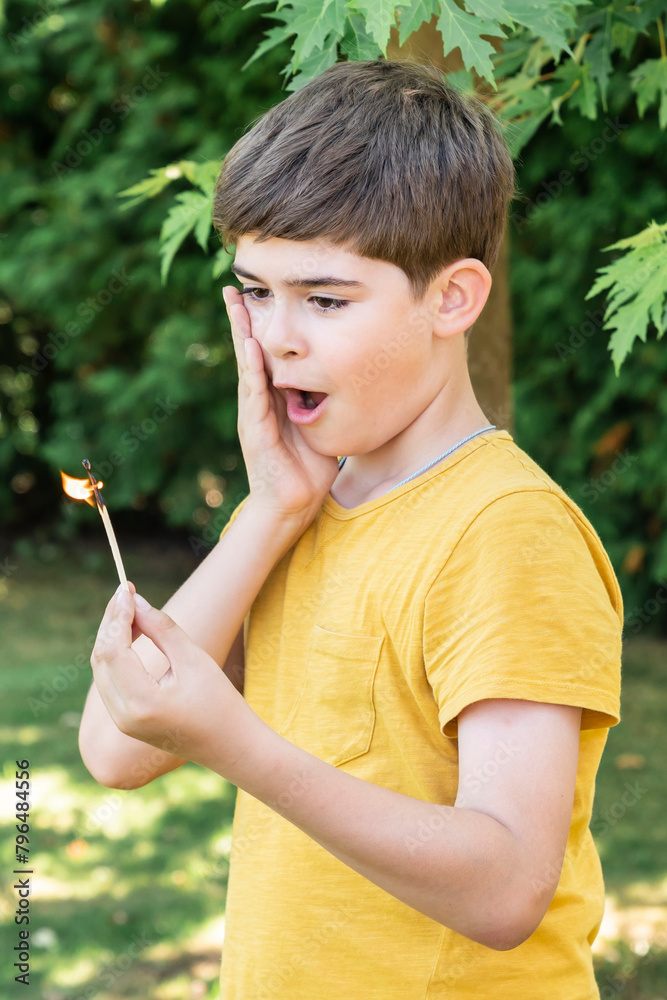 Little naughty boy holds burning match in hands and plays with fire on the backyard Little naughty boy holds burning match in hands and plays with fire on the backyard