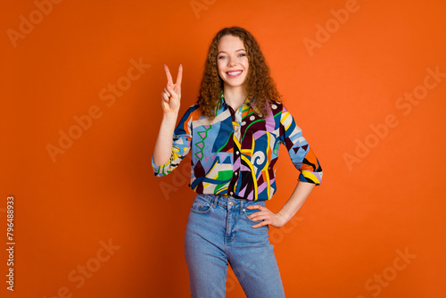Photo of lovely cheerful nice girl wear stylish print clothes demonstrate v-sign isolated on vivid orange color background