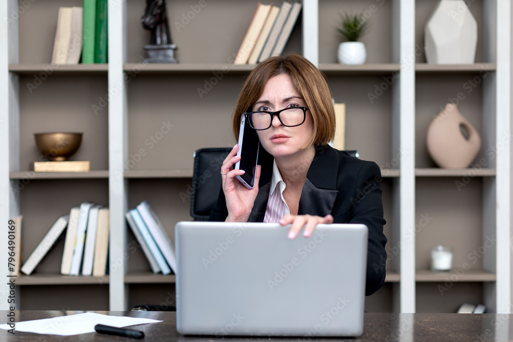Shocked business woman looking at laptop and talking to mobile phone. She discussing problems in business Shocked business woman looking at laptop and talking to mobile phone. She discussing problems in business