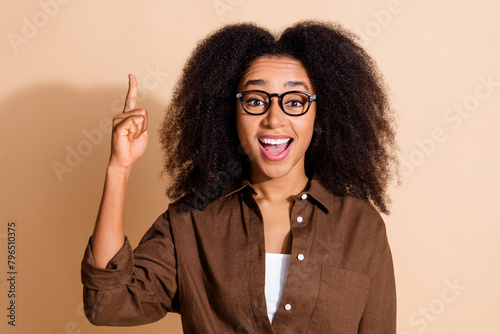 Photo of clever girl with perming coiffure wear brown blouse in glasses raising finger have idea isolated on pastel color background